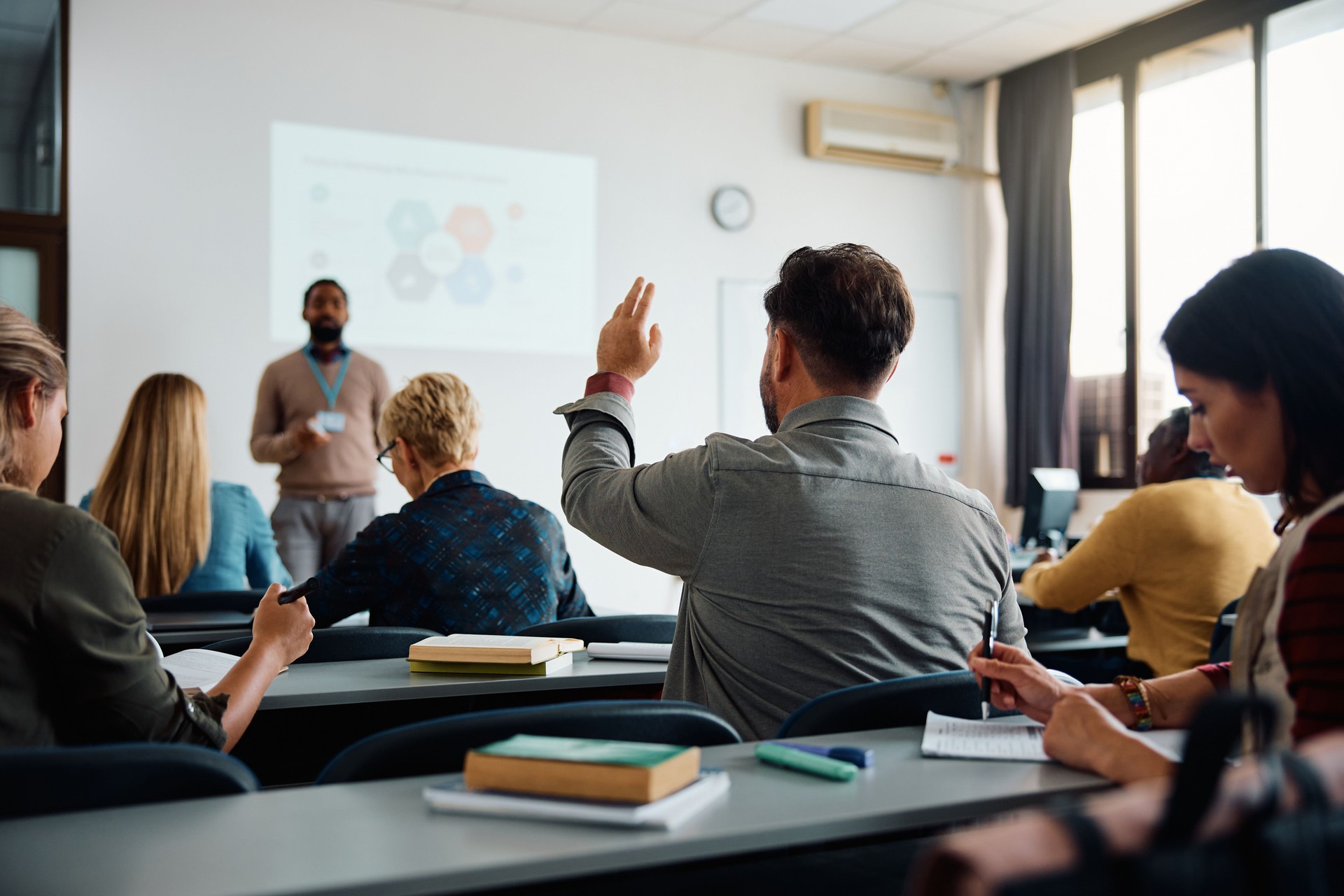 Back view of student raising his hand to answer teacher's question during education training class.